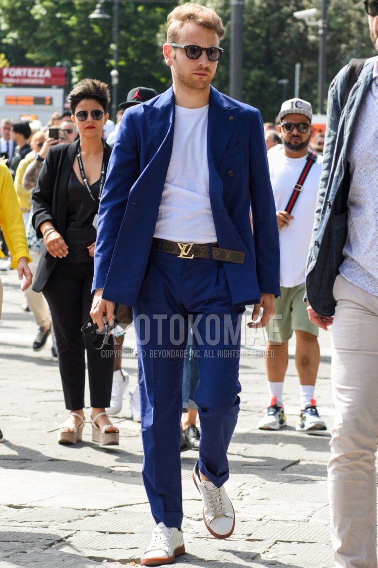 Men's coordinate and outfit with plain black sunglasses, plain white t-shirt, Louis Vuitton brown decal logo leather belt, white low-cut sneakers, and plain blue suit.