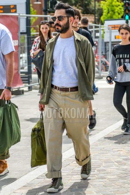 Men's outfit/clothing with solid color sunglasses, olive green solid color shirt jacket, gray solid color t-shirt, brown solid color leather belt, beige solid color wide pants, olive green high cut sneakers, olive green solid color briefcase/handbag.