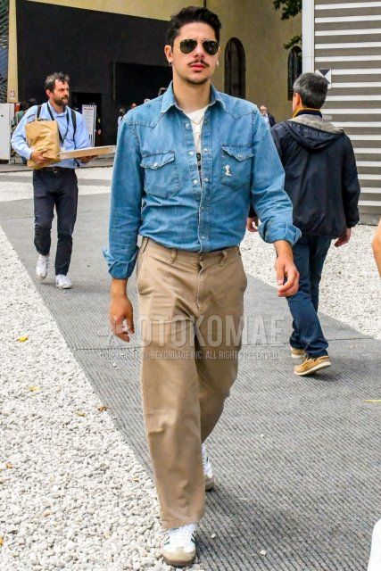 Men's coordinate and outfit with solid color sunglasses, solid color blue denim/chambray shirt, solid color white t-shirt, solid color beige cotton pants, solid color beige wide pants, solid color beige chinos, and white Adidas sneakers.