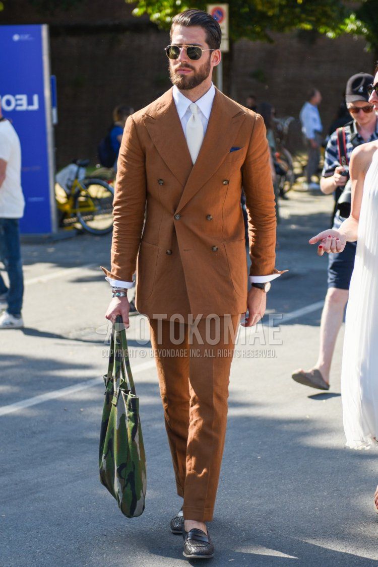 Men's coordination and outfit with plain gold/black sunglasses, plain white shirt, multi-colored camouflage tote bag, plain brown suit, and plain white tie.