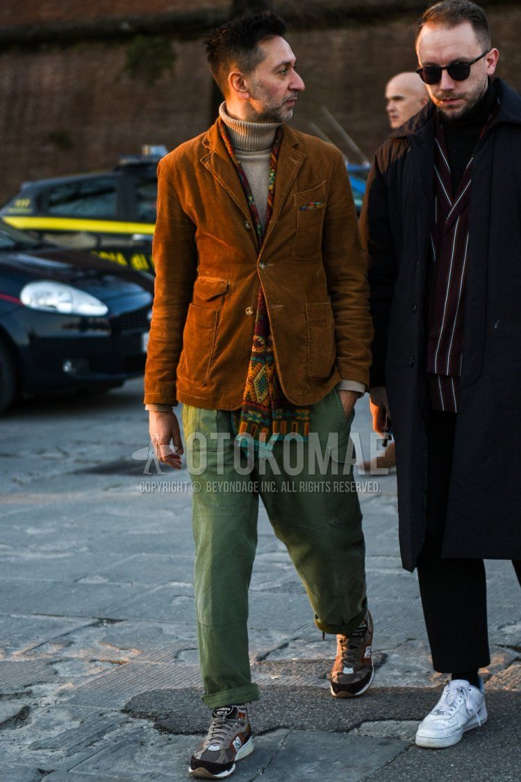 Men's fall/winter outfit with multi-colored scarf/stall, plain brown tailored jacket, plain beige turtleneck knit, plain olive green cargo pants, and New Balance gray low-cut sneakers.
