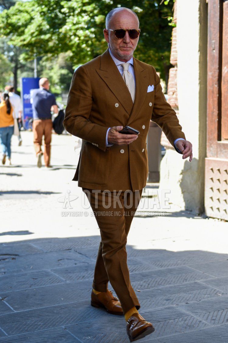 Men's coordinate and outfit with beige tortoiseshell sunglasses, plain white shirt, plain yellow socks, brown monk shoes leather shoes, plain brown suit and beige necktie.