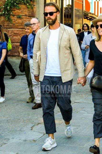 Men's coordinate and outfit with solid color sunglasses, solid color beige shirt, solid color white t-shirt, solid color black ankle pants, solid color black wide pants, and beige low-cut sneakers.