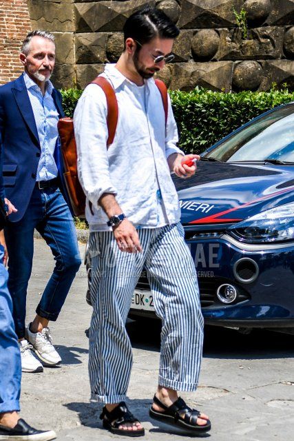 Men's coordinate and outfit with plain silver sunglasses, plain white shirt, plain white t-shirt, wide white/navy striped pants, black leather sandals, and plain brown backpack.