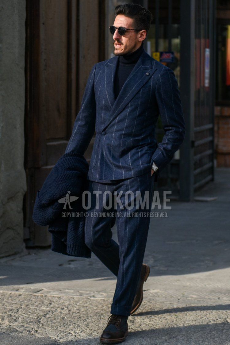 Men's fall/spring coordination and outfit with brown tortoiseshell sunglasses, plain black turtleneck knit, brown boots, and navy striped suit.
