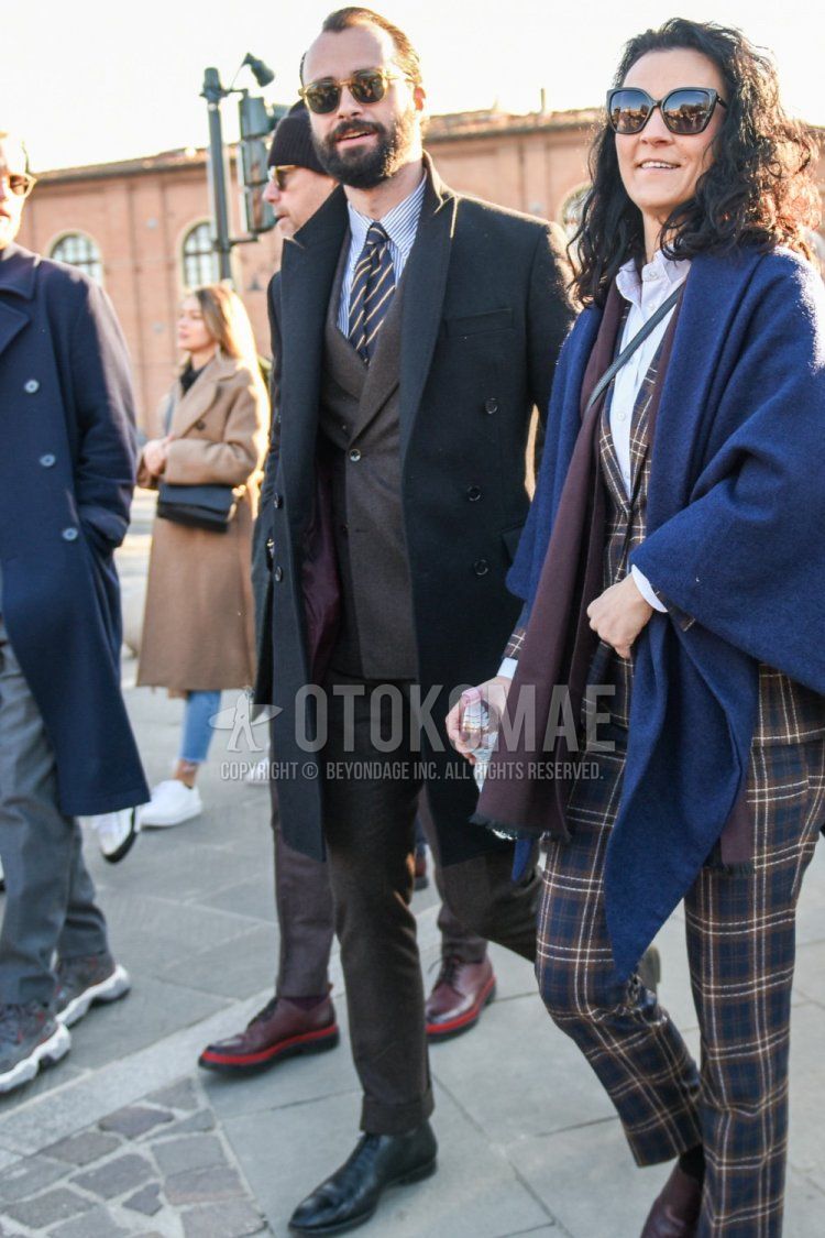 Men's fall/winter outfit with plain brown sunglasses, plain dark gray chester coat, white/blue striped shirt, black straight tip leather shoes, plain brown suit, navy/yellow/brown regimental tie.