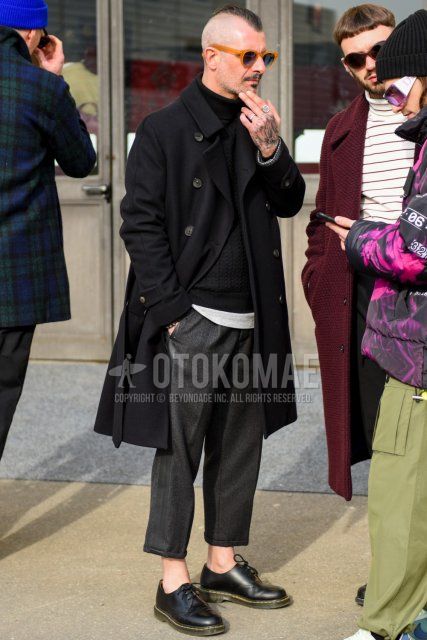 Men's fall/winter outfit with solid beige sunglasses, solid black trench coat, solid black turtleneck knit, solid green t-shirt, solid gray slacks, solid gray cropped pants, and Dr. Martens black plain toe leather shoes.