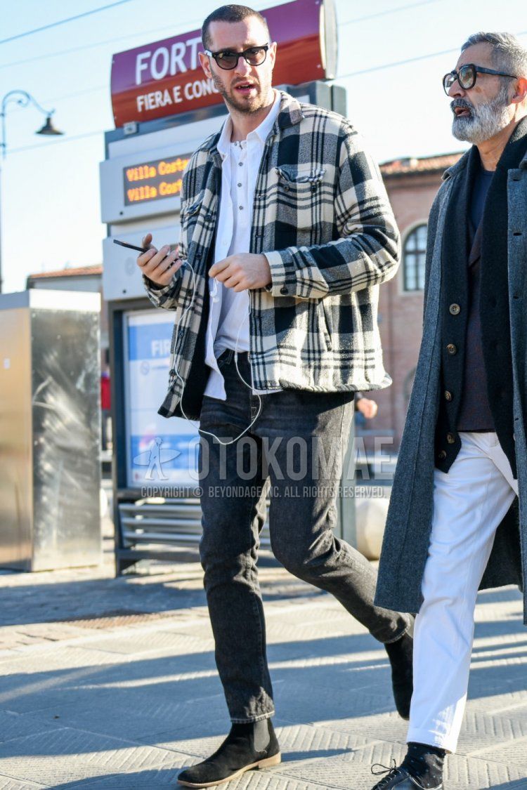Men's winter/fall outfit with plain black sunglasses, white/black checked shirt jacket, plain white shirt, plain white t-shirt with henley neck, plain gray denim/jeans, plain gray cropped pants, suede black side gore boots.