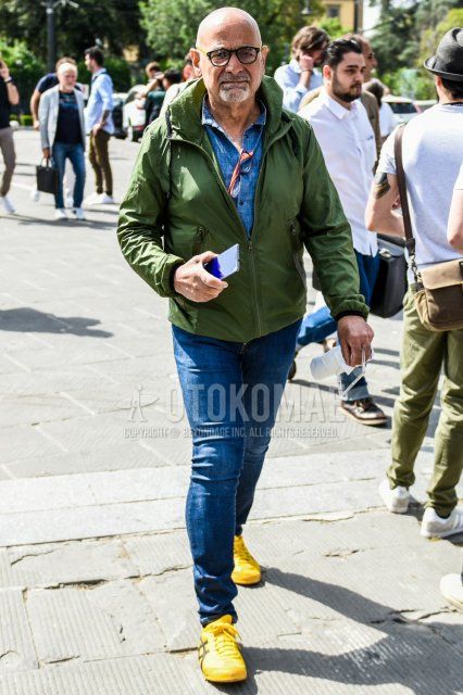 Men's coordinate and outfit with solid black/yellow glasses, solid orange windbreaker, solid blue denim/chambray shirt, solid blue denim/jeans, and Onitsuka Tiger yellow-cut sneakers.