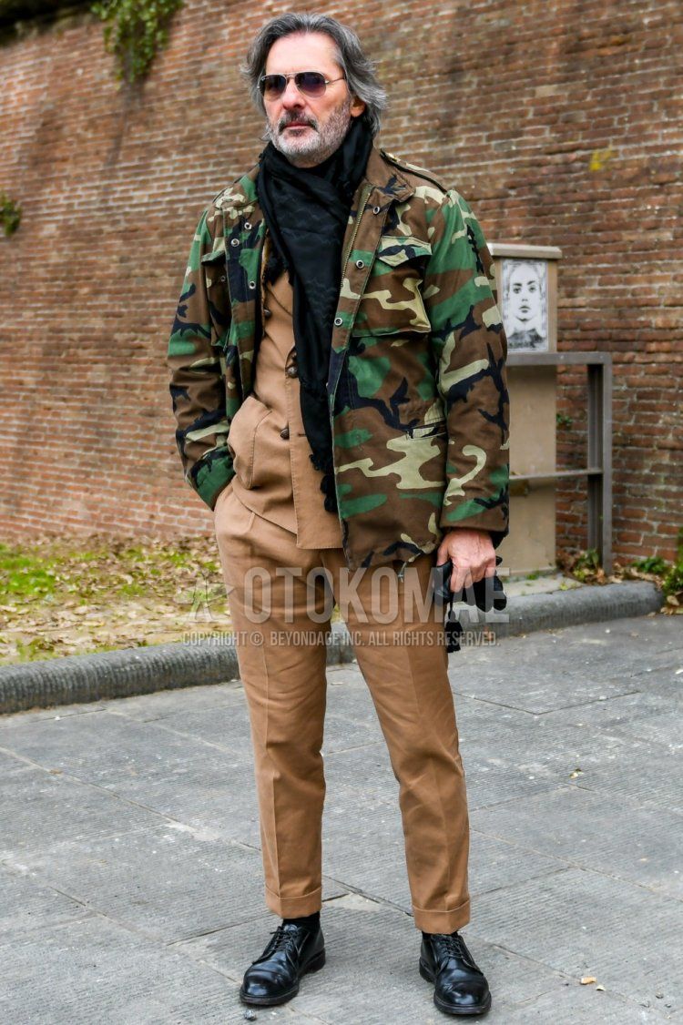 Men's coordinate and outfit with Ray-Ban teardrop plain silver sunglasses, black scarf/stall, olive green/brown camouflage M-65, plain black socks, black plain toe leather shoes, and plain beige suit.