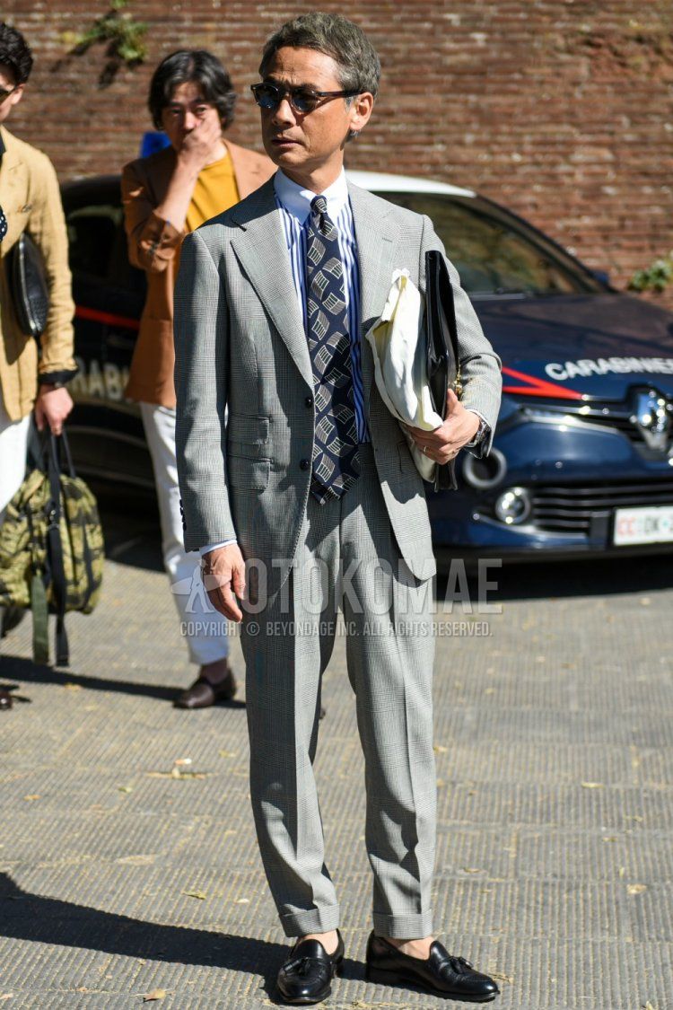Men's coordinate and outfit with blue/white striped shirt, black tassel loafer leather shoes, plain black clutch bag/second bag/drawstring, plain gray suit and navy tie.