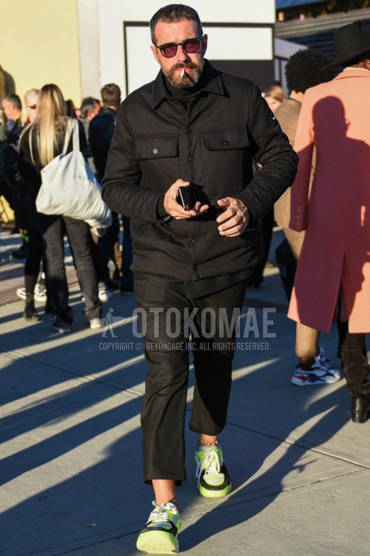 Men's fall/spring outfit with plain black sunglasses, plain black shirt jacket, plain black turtleneck knit, plain black cropped pants, plain black cotton pants, and yellow low-cut sneakers.