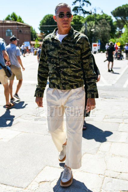 Men's coordinate and outfit with teardrop silver/black plain sunglasses, green camouflage trucker jacket, plain white t-shirt, plain white wide-leg pants, plain white cotton pants, and white low-cut sneakers.