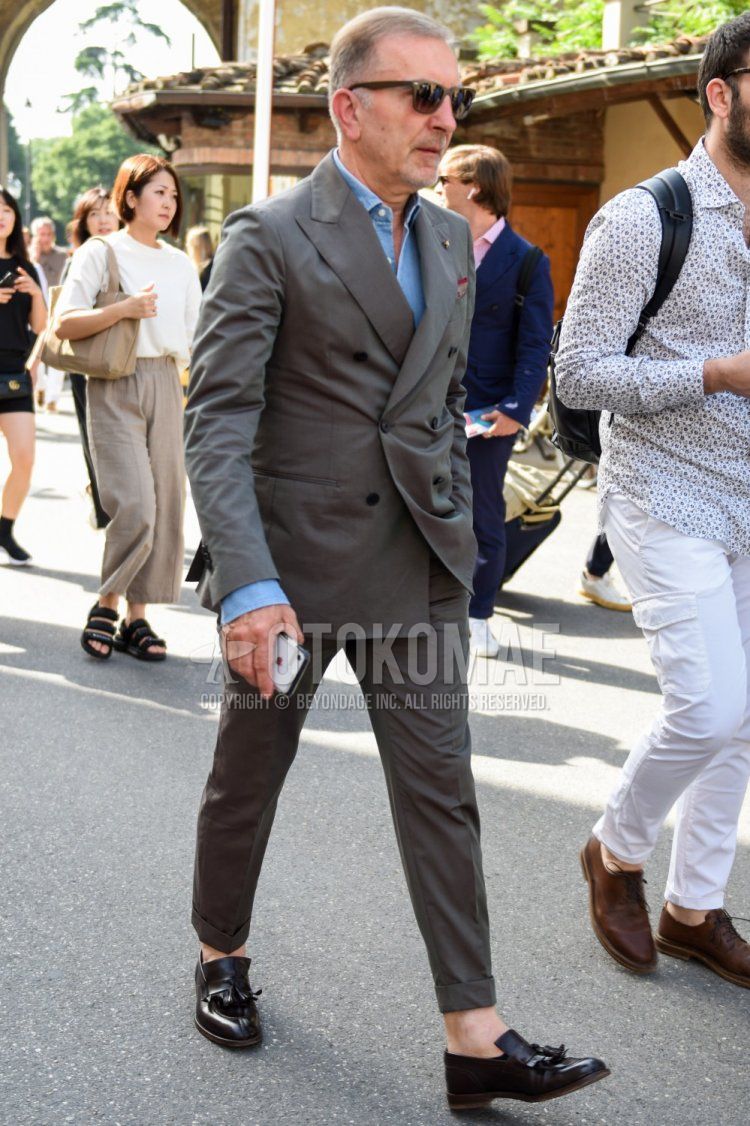 Men's coordinate and outfit with plain brown sunglasses, plain light blue denim/chambray shirt, black tassel loafer leather shoes, and plain gray suit.