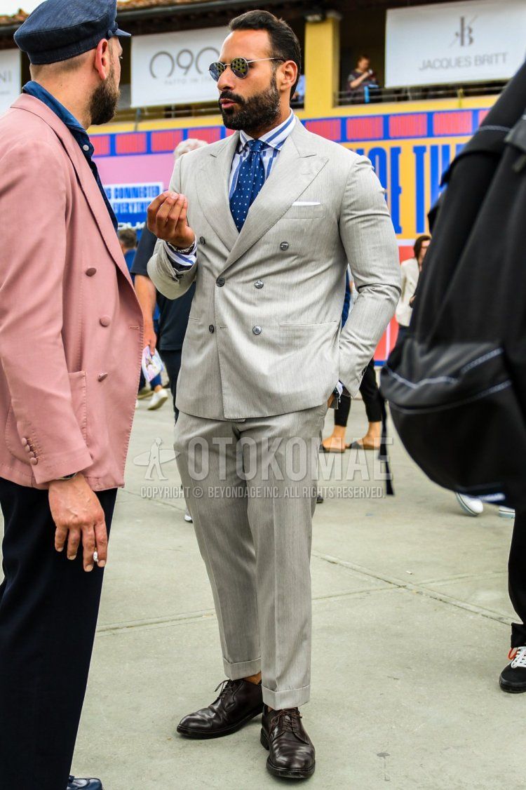 Men's coordination and outfit with plain sunglasses, white/blue striped shirt, brown plain toe leather shoes, plain gray suit, and blue dot tie.
