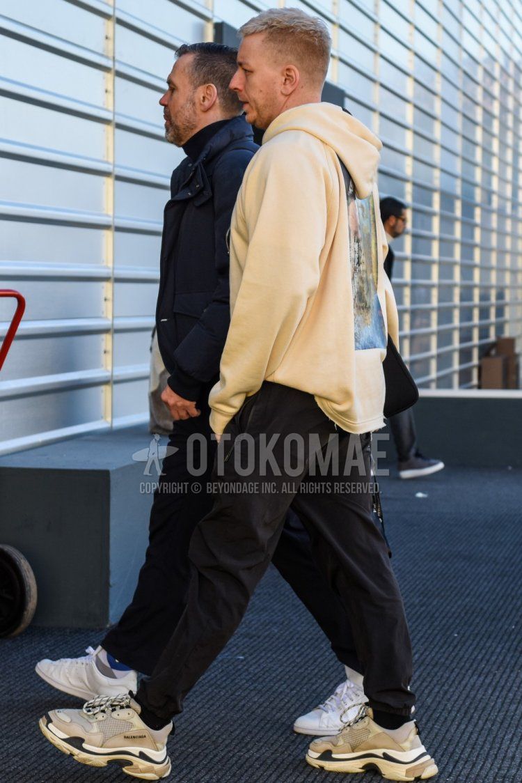 Men's spring/autumn coordinate and outfit with beige graphic hoodie, plain black jogger pants/ribbed pants, and Balenciaga Triple S gray low-cut sneakers.
