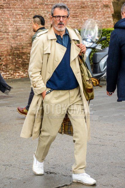 Men's winter/fall/spring coordinate and outfit with plain black glasses, plain beige trench coat, plain navy shirt, plain navy sweater with v-neck, plain beige chinos, and white low-cut Reebok sneakers.