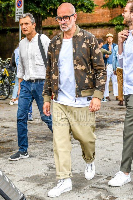 Men's coordinate and outfit with plain black glasses, brown/beige camouflage MA-1, plain white T-shirt, plain beige chinos, plain beige wide pants, and white high-cut sneakers.