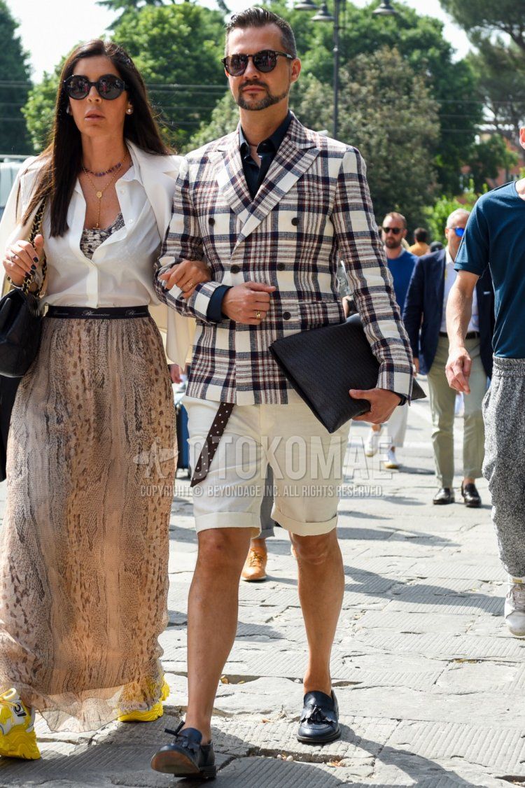 Men's outfit and outfit with plain black sunglasses, white/multi-colored checked tailored jacket, plain navy shirt, brown dotted tape belt, plain white shorts, navy bit loafer leather shoes, and plain black clutch/second bag/drawstring bag.