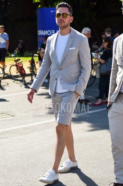 Men's coordinate and outfit with plain black/yellow sunglasses, plain gray tailored jacket, plain white t-shirt, plain gray shorts, and white low-cut sneakers.