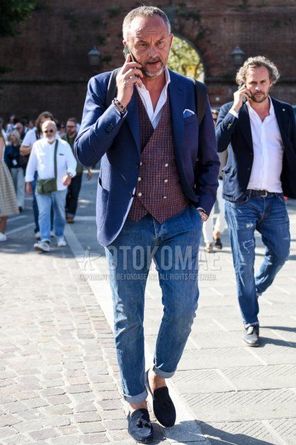 Men's coordinate and outfit with plain navy tailored jacket, plain white shirt, brown checked gilet, plain blue denim/jeans, and navy tassel loafer leather shoes.