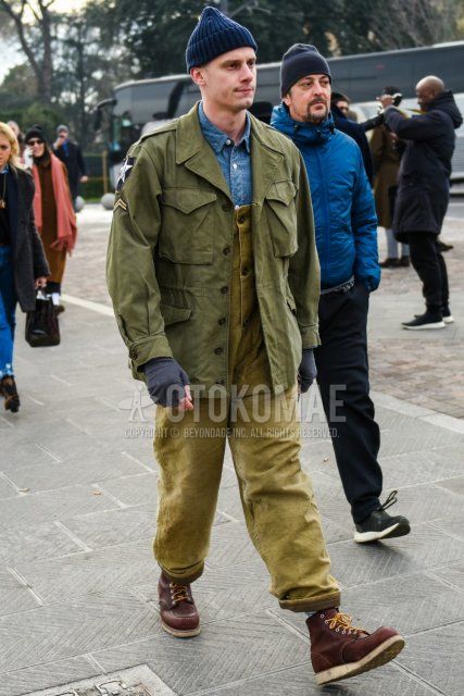 Men's coordinate and outfit with solid navy knit cap, solid olive green M-65, overalls solid beige jumpsuit, solid blue denim/chambray shirt, and brown work boots.