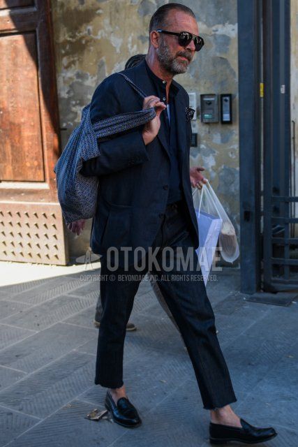 Men's coordinate and outfit with plain black sunglasses, plain black tailored jacket, plain black shirt, plain black denim/jeans, plain black coin loafer leather shoes, and gray bag tote bag.