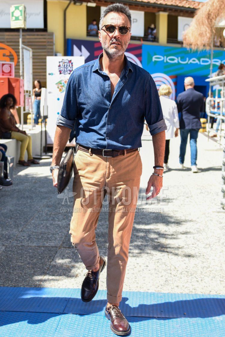 Brown tortoiseshell sunglasses with thermons, solid blue denim/chambray shirt, solid brown mesh belt, solid brown leather belt, solid beige chinos, brown plain toe leather shoes, solid black clutch/second bag/drawstring, spring/fall/summer Men's Codes and Outfits.