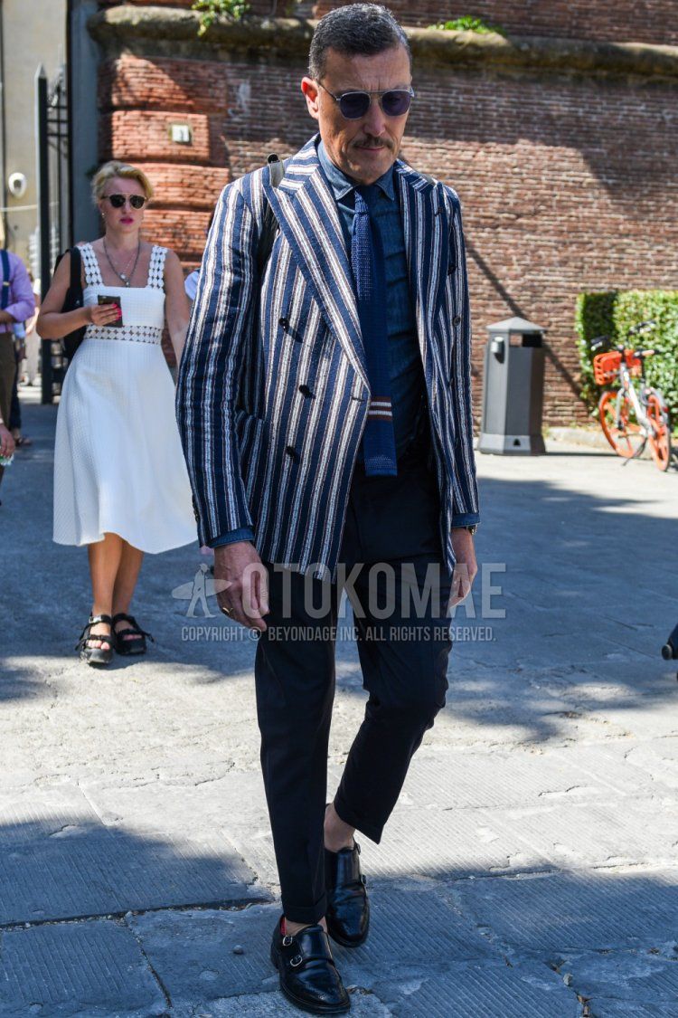 Men's coordinate and outfit with clear/gray solid color sunglasses, white/navy striped tailored jacket, blue solid color denim/chambray shirt, navy/black solid color slacks, black monk shoe leather shoes, and blue solid color knit tie.