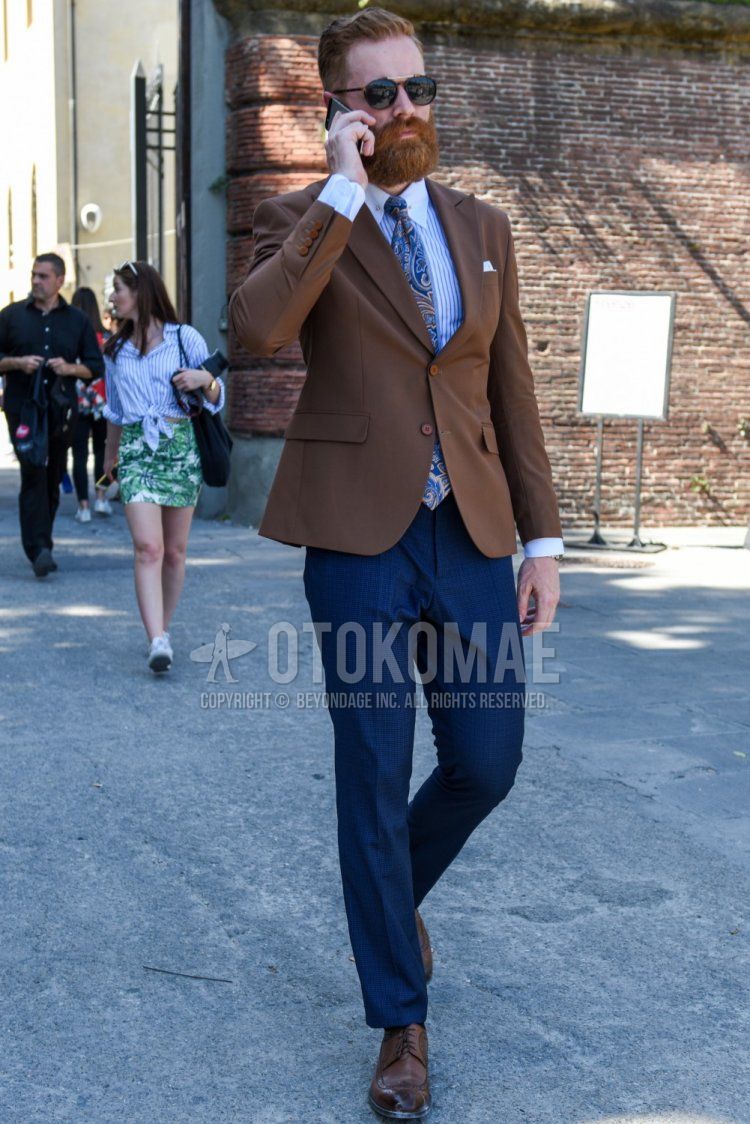 Men's coordinate and outfit with plain black sunglasses, plain brown tailored jacket, light blue striped shirt, plain navy slacks, brown brogue shoes leather shoes, and blue tie tie.