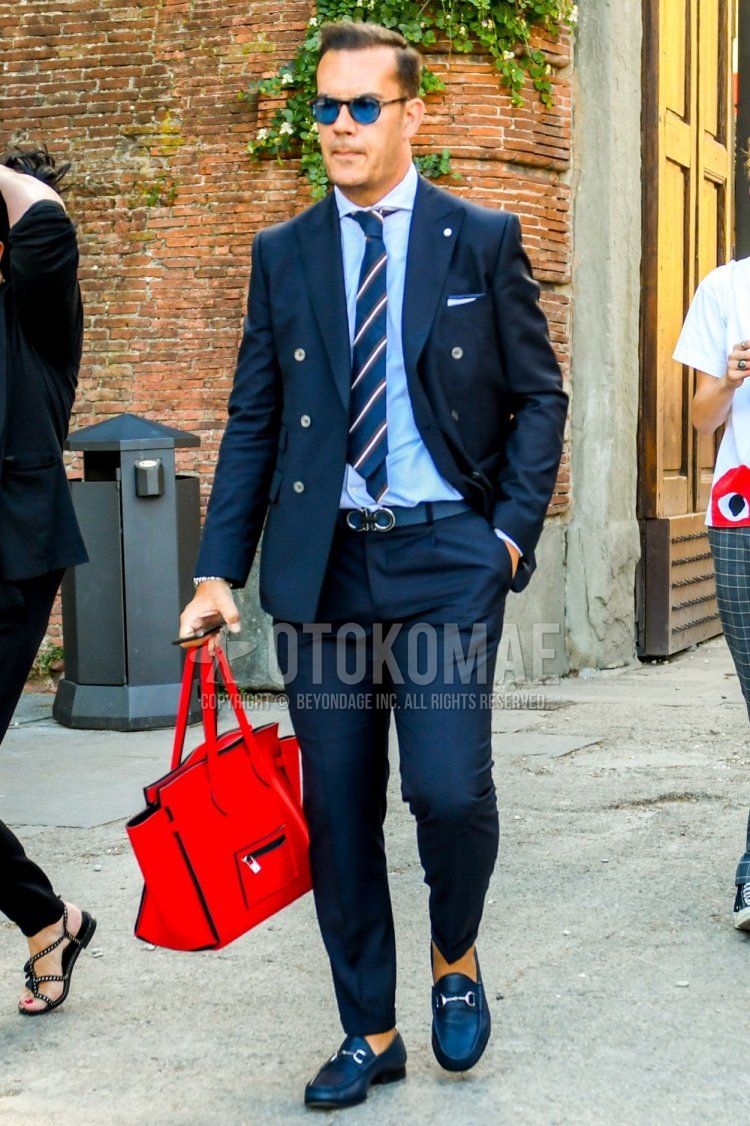 Men's coordinate and outfit with plain sunglasses, plain white shirt, plain red briefcase/handbag, plain navy suit and navy regimental tie.