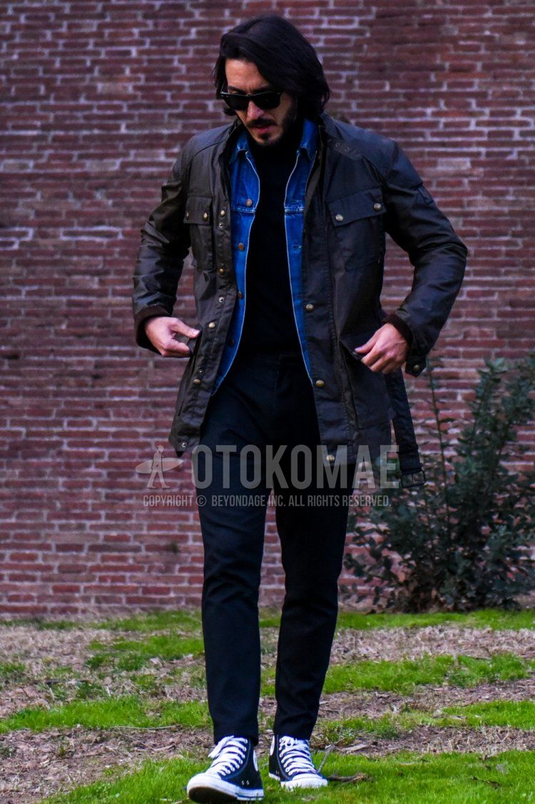 Men's coordinate and outfit with plain black sunglasses, plain black Belstaff rider's jacket, plain blue denim jacket, plain black sweater, plain black denim/jeans, and black high-cut sneakers.