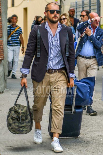 Ray-Ban Wayfarer solid color sunglasses, navy solid color tailored jacket, white/blue striped shirt, brown solid color leather belt, beige solid color chinos, Adidas Stan Smith white low cut sneakers, green/black camo briefcase/handbag Men's coordinate/outfit with.