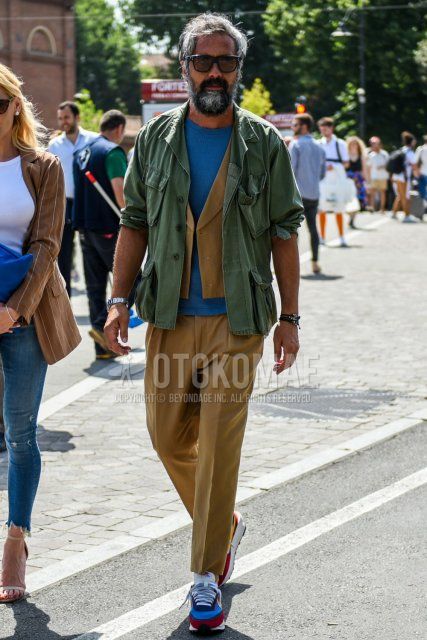 Men's coordinate and outfit with plain black sunglasses, plain olive green M-65, plain blue t-shirt, plain brown gilet, plain brown ankle pants, plain white socks, and multi-colored low-cut sneakers.
