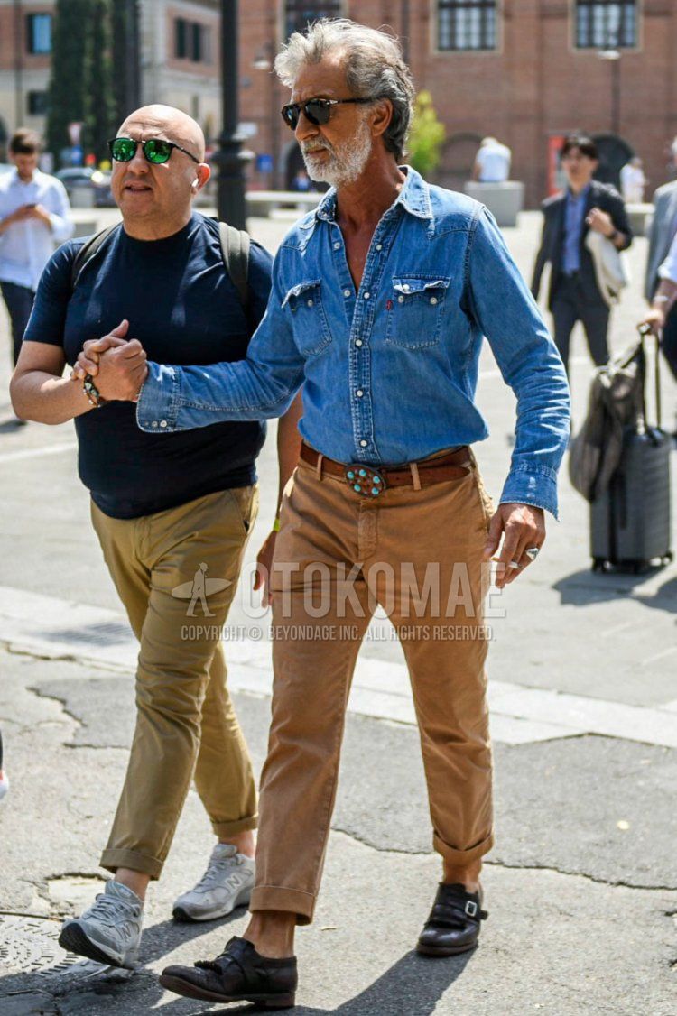 Men's coordinate and outfit with solid black sunglasses, solid blue denim/chambray shirt, solid brown leather belt, solid brown cotton pants, and brown monk shoe leather shoes.