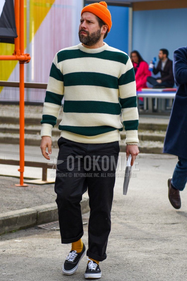 Men's fall/spring/winter outfit with plain orange knit cap, white/green top/inner sweater, plain black slacks, plain yellow socks, and black low-cut sneakers by Vans.