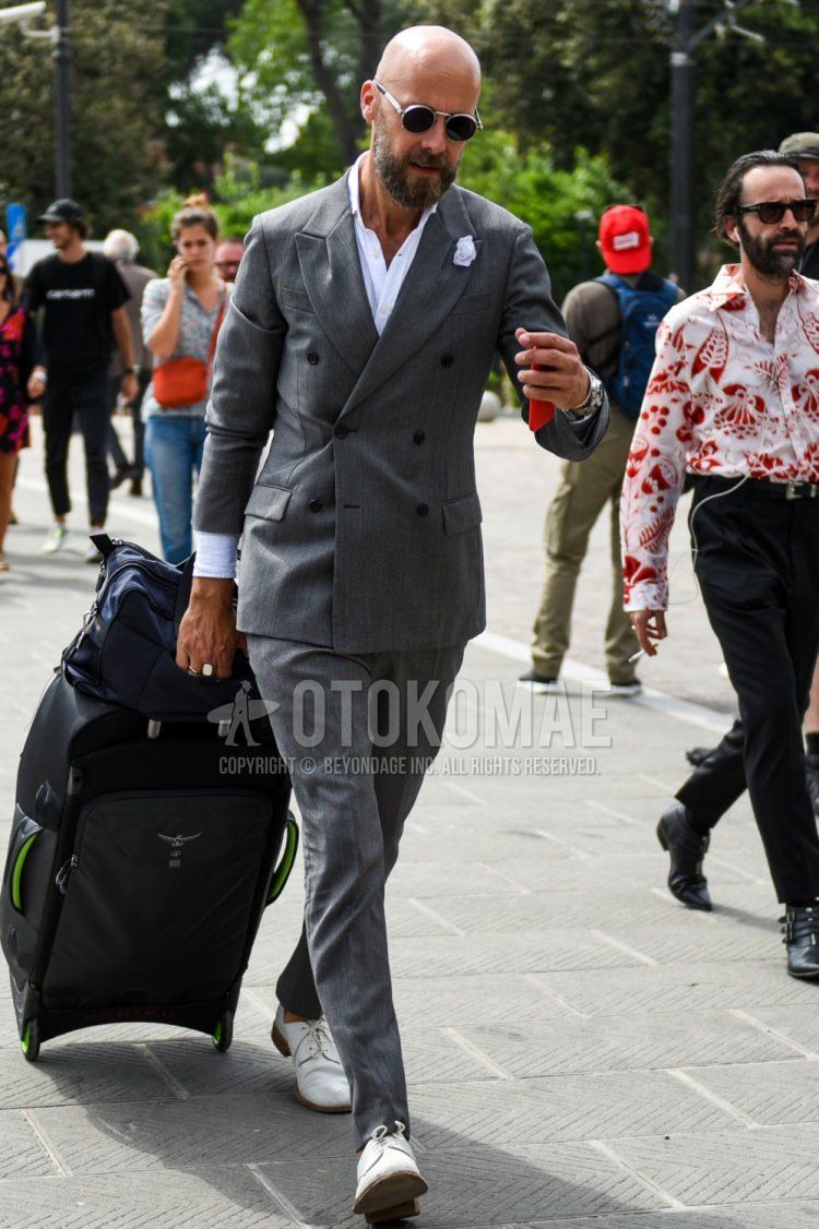 Men's coordinate and outfit with plain sunglasses, plain white shirt, white plain toe leather shoes, plain black suitcase, and plain gray suit.