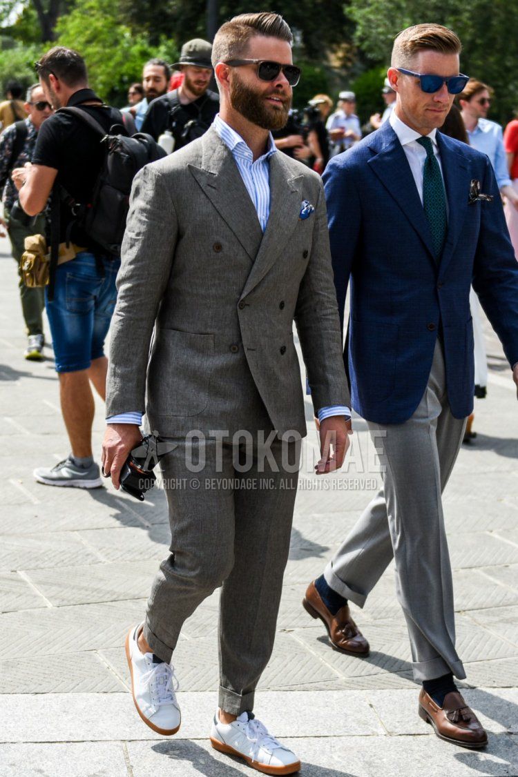 Men's coordinate and outfit with plain brown sunglasses, light blue striped shirt, white low-cut sneakers, and plain gray suit.