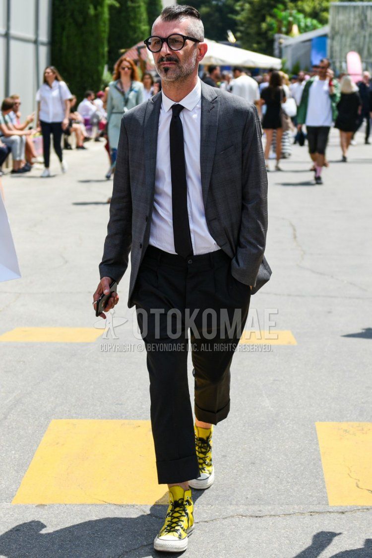 Men's coordinate and outfit with plain black glasses, gray checked tailored jacket, plain white shirt, plain gray slacks, Converse All Star yellow high-cut sneakers, and plain black tie.