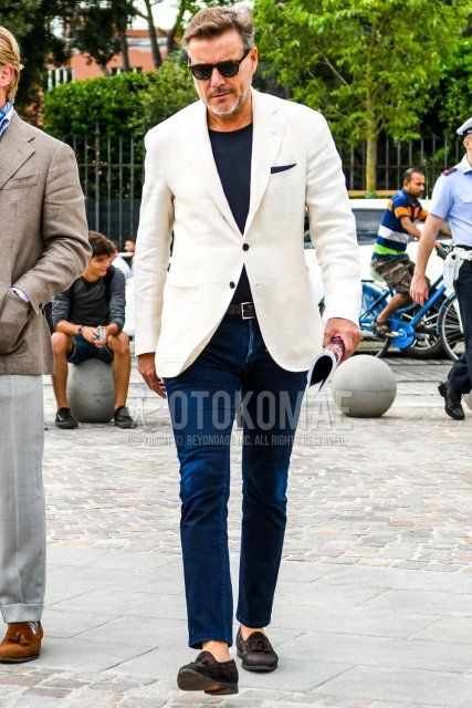 Men's coordinate and outfit with brown tortoiseshell sunglasses, plain white tailored jacket, plain navy t-shirt, plain brown leather belt, plain navy denim/jeans, and suede brown tassel loafer leather shoes.