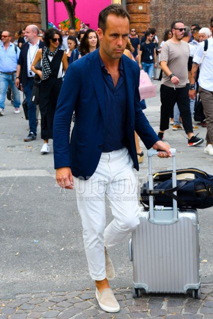 Men's spring, summer, and fall outfits with plain navy tailored jacket, plain navy polo shirt, plain white ankle pants, plain white beltless pants, beige slip-on sneakers, plain navy briefcase/handbag, and plain silver suitcase.