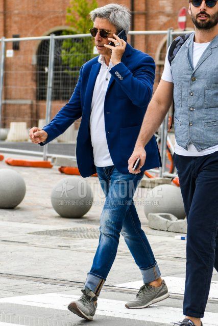 Men's coordinate and outfit with tortoiseshell sunglasses, plain blue tailored jacket, plain white polo shirt, plain blue denim/jeans, and New Balance gray low-cut sneakers.