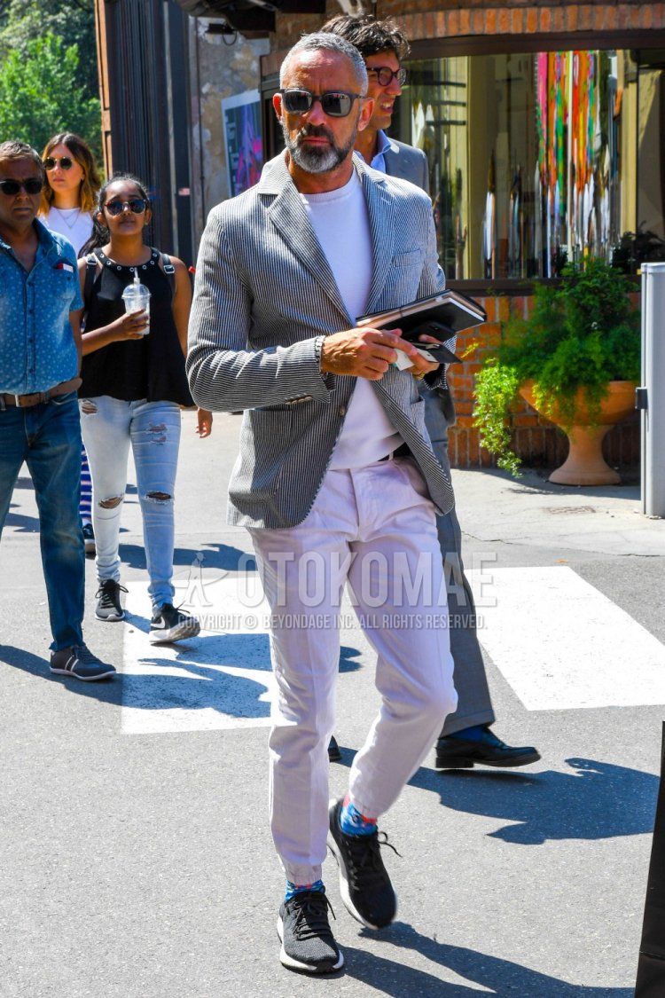 Men's coordinate and outfit with plain sunglasses, black and white striped tailored jacket, plain white sweater, plain white jogger pants/ribbed pants, blue graphic socks, and dark gray low-cut sneakers.
