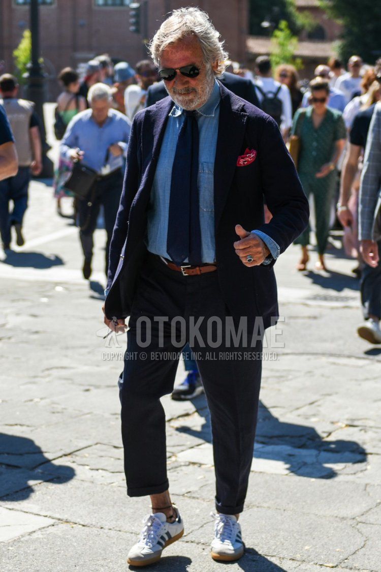Teardrop Ray-Ban Aviator solid black sunglasses, solid navy tailored jacket, solid light blue denim/chambray shirt, solid dark gray slacks, solid ankle pants, Adidas Country white low cut sneakers, solid navy tie Men's coordinate/outfit.