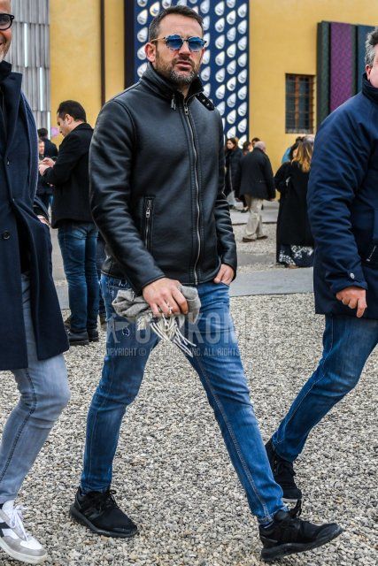 Men's coordinate and outfit with solid color sunglasses, solid color black leather jacket (other than rider's), solid color blue denim/jeans, and black low-cut sneakers.
