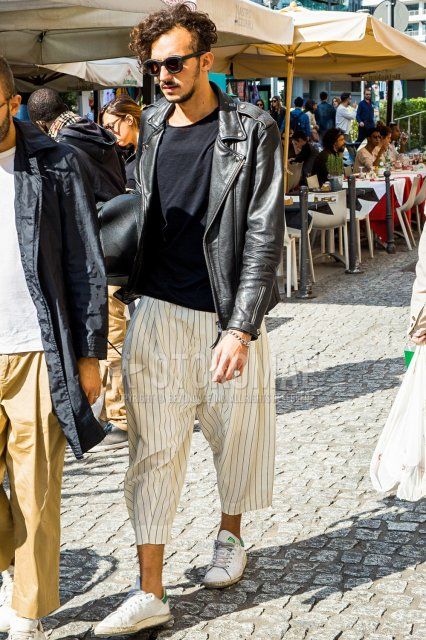 Men's fall/spring outfit with plain black sunglasses, plain black rider's jacket, plain black t-shirt, beige striped sarouel pants, beige striped cropped pants, and Adidas Stan Smith white low-cut sneakers.