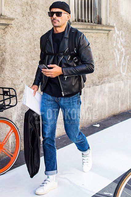 Men's fall/spring outfit with solid black knit cap, solid black sunglasses, solid black rider's jacket, solid black sweater, solid blue denim/jeans, solid white socks, and Adidas Stan Smith white low-cut sneakers.