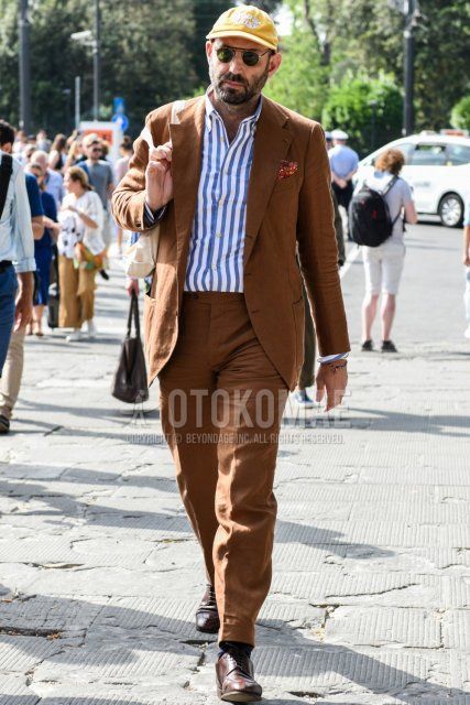 Men's spring, summer, and fall coordinate and outfit with yellow graphic baseball cap, solid black sunglasses, solid light blue shirt, solid black socks, brown U-tip leather shoes, and solid brown suit.