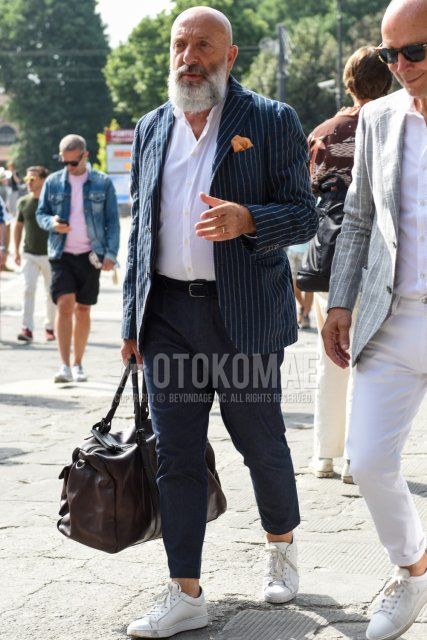 Spring and fall men's coordinate and outfit with navy striped tailored jacket, plain white shirt, plain black leather belt, plain gray slacks, white low-cut sneakers, and plain brown Boston bag.