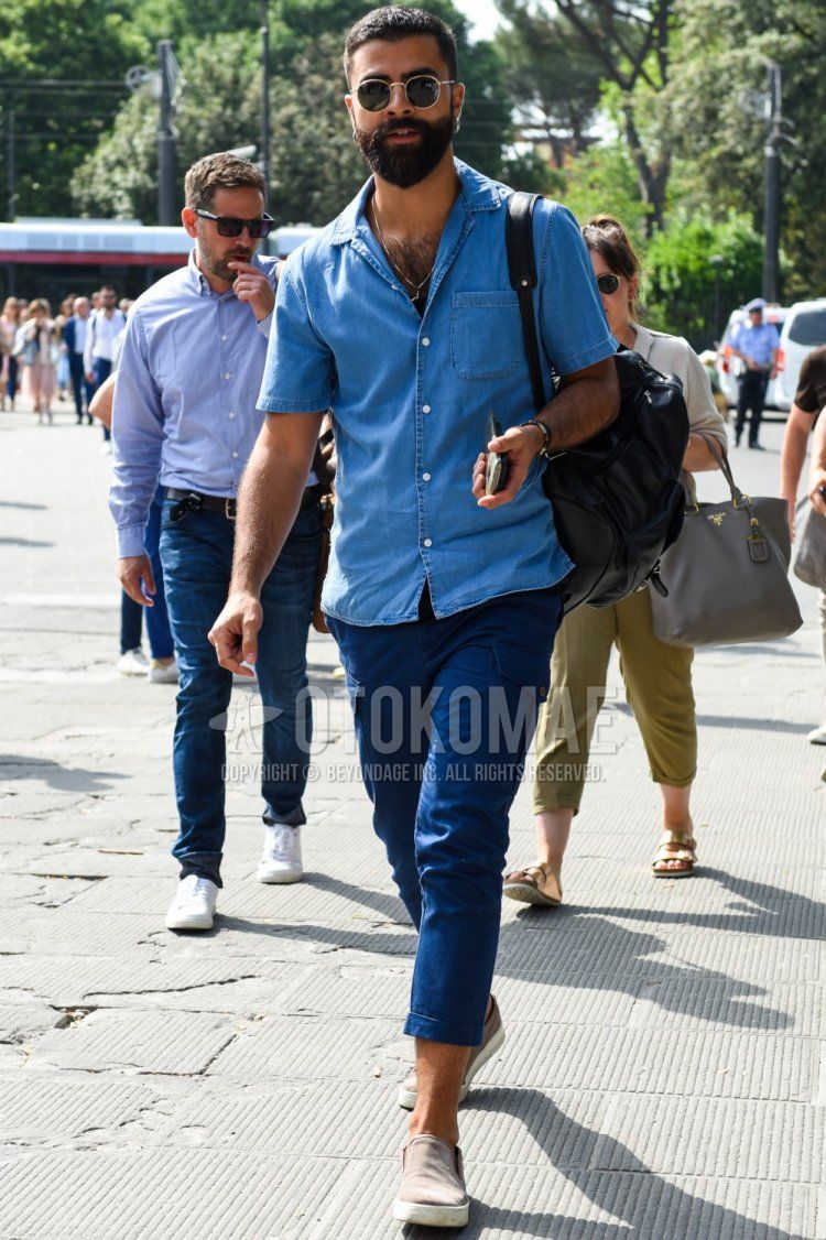 Summer men's coordinate and outfit with gold solid color sunglasses, open collar blue solid color denim/chambray shirt, blue solid color cargo pants, and beige low cut sneakers.